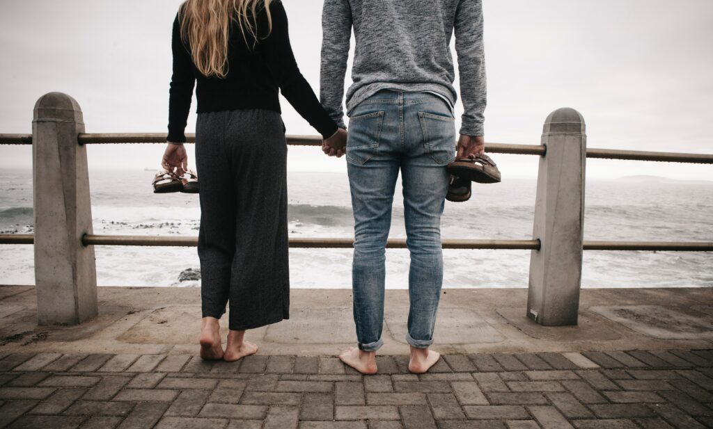 Ein Paar steht auf einer Promenade, Hand in Hand und schaut auf das Meer.